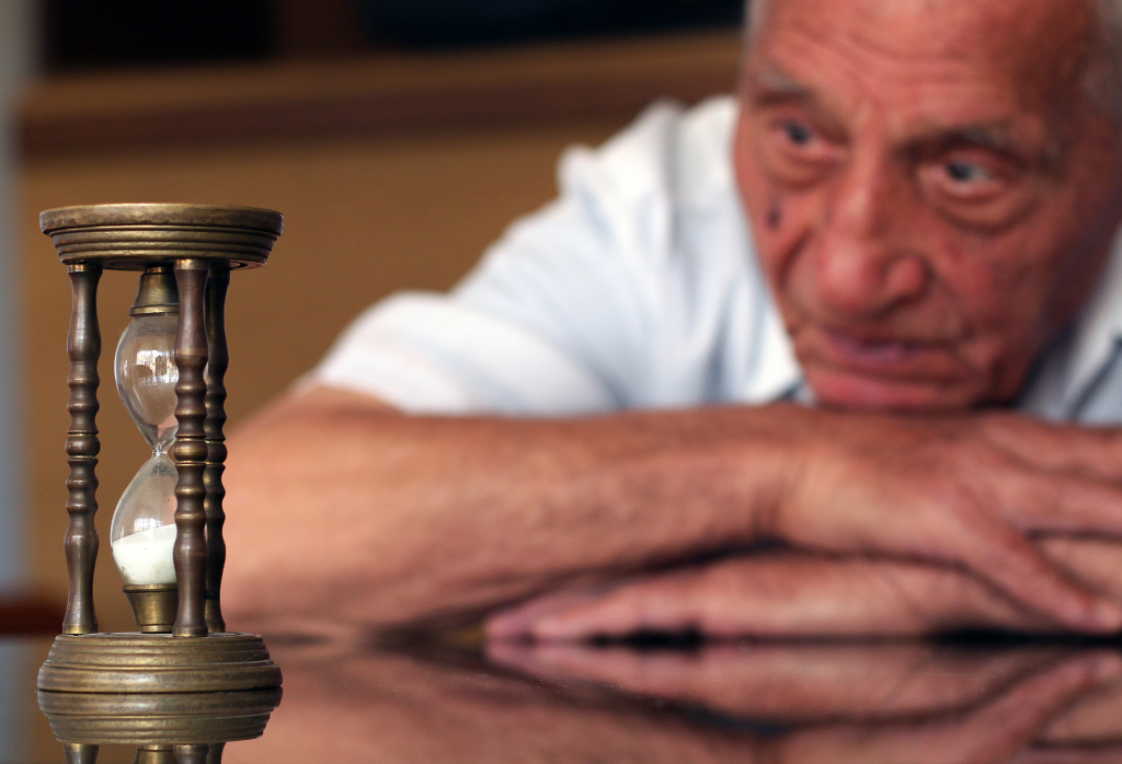 Old man looking at hourglass sand timer.