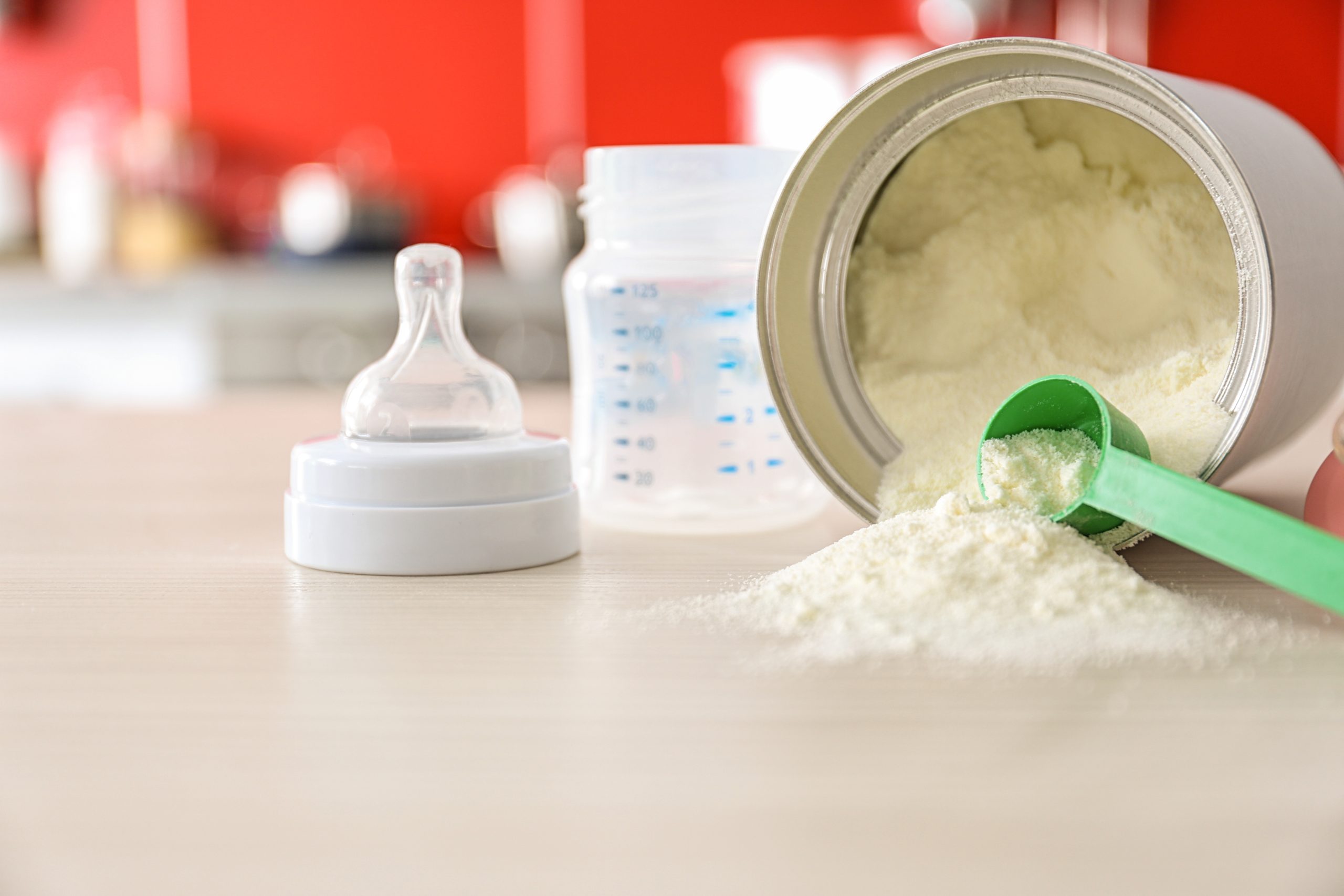 Baby milk formula on kitchen counter with baby bottle in the background.